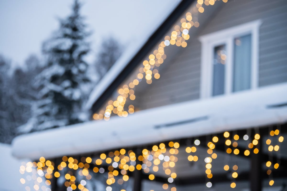 Snowy blurred winter house in forest with bokeh of festive Christmas lights on creating dreamy holiday atmosphere and warm seasonal background. Celebration themes.